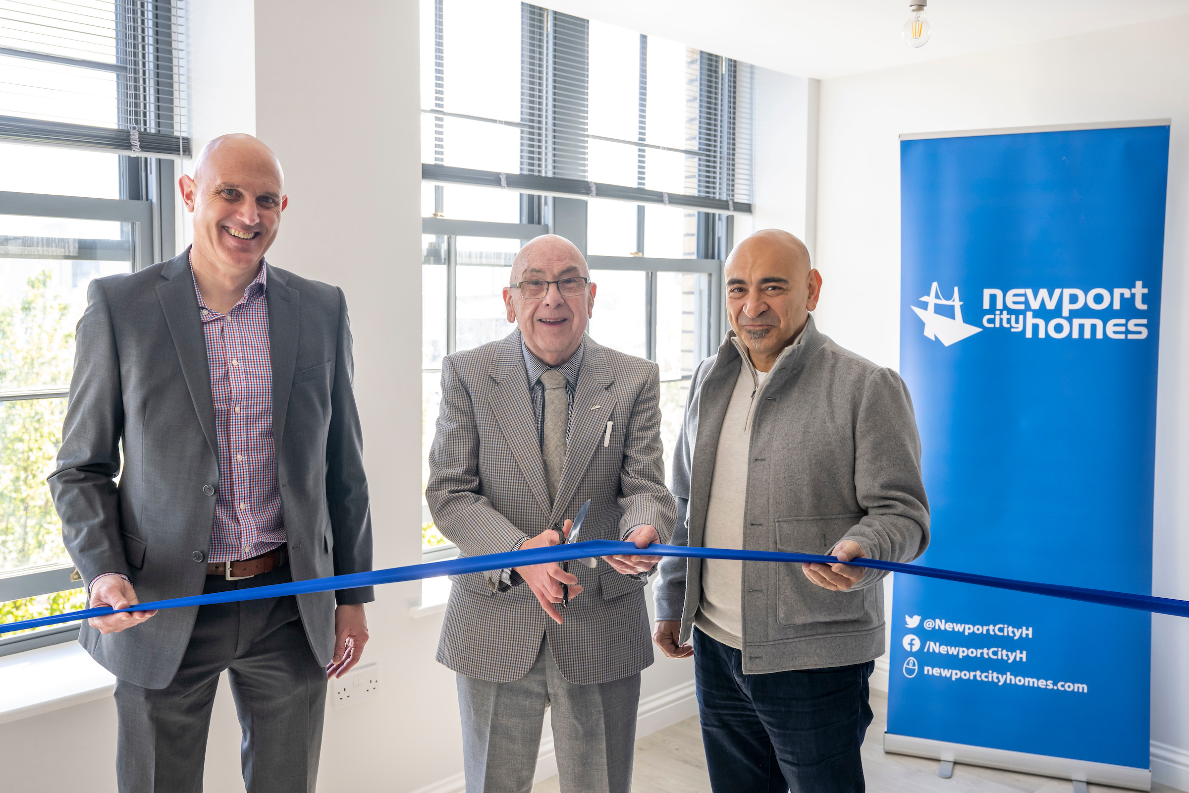 three men cut a ribbon to celebrate a new housing development