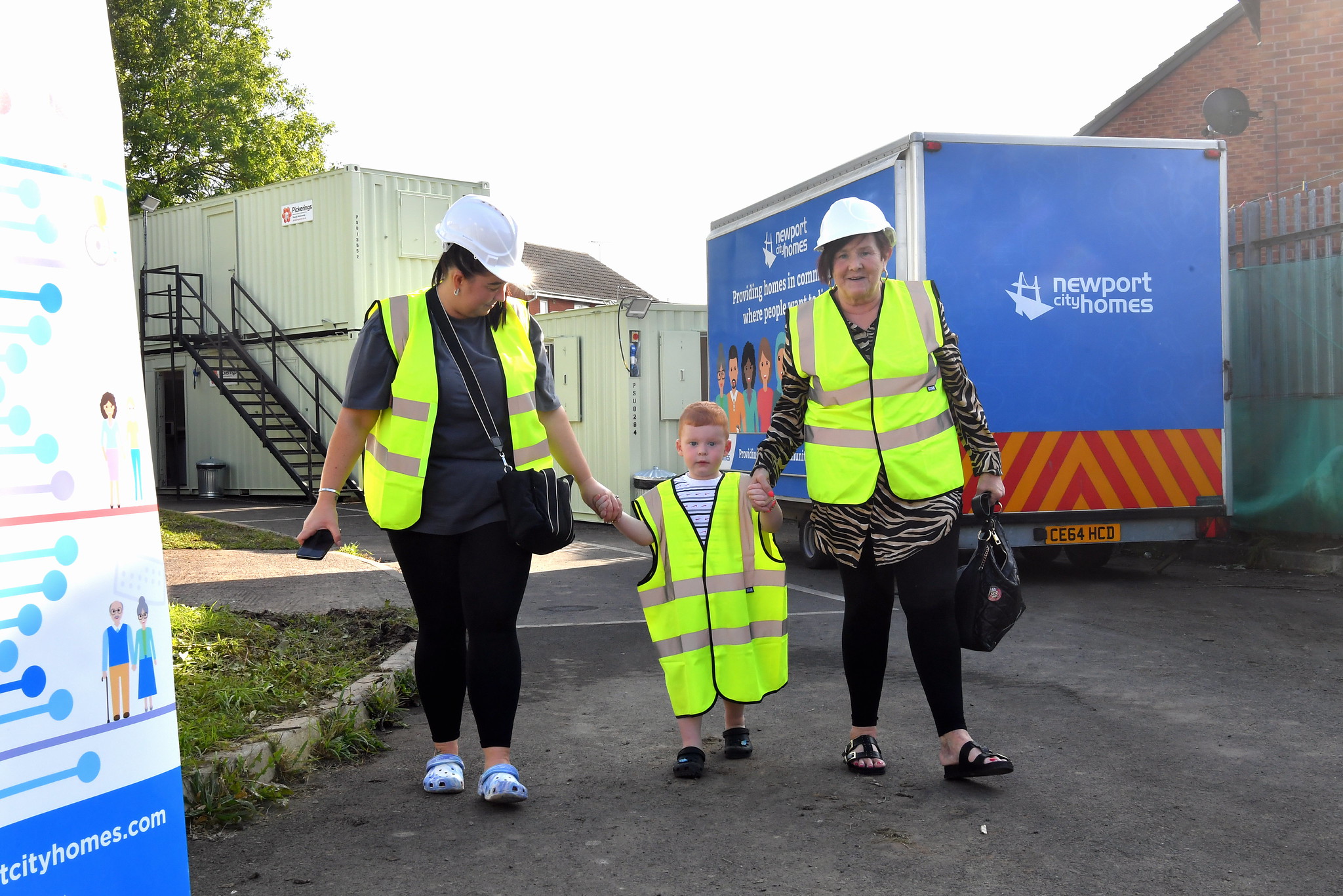 Two women walk with a child through the grounds of the energy centre wearing hig-vis vesta and hard hats
